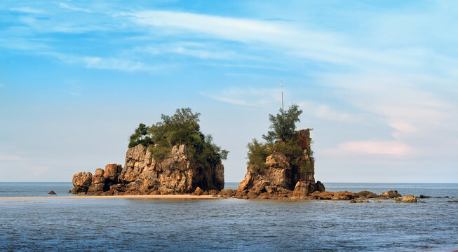 Scenic view of dramatic rocky cliffs, a quiet sandy beach, and calm blue sea under a bright tropical sky in Pantai Kuala Kemasik, Terengganu, Malaysia