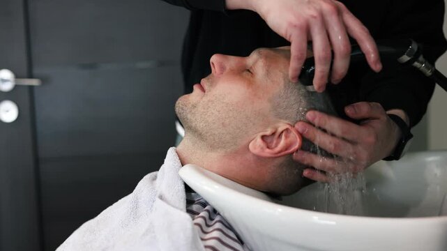 A young male Barber adjusts the hair of a male client. Professional hair care products. Cinematic close-up of a barber giving fade haircut to male client. Slow motion shot of short clipper hairstyle.