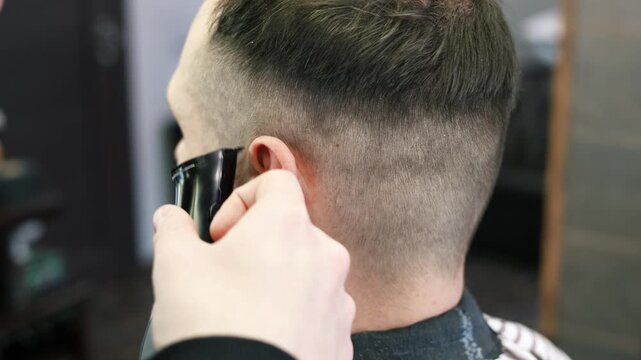 A young male Barber adjusts the hair of a male client. Professional hair care products. Cinematic close-up of a barber giving fade haircut to male client. Slow motion shot of short clipper hairstyle.