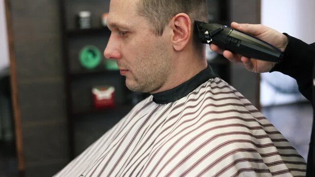 A young male Barber adjusts the hair of a male client. Professional hair care products. Cinematic close-up of a barber giving fade haircut to male client. Slow motion shot of short clipper hairstyle.