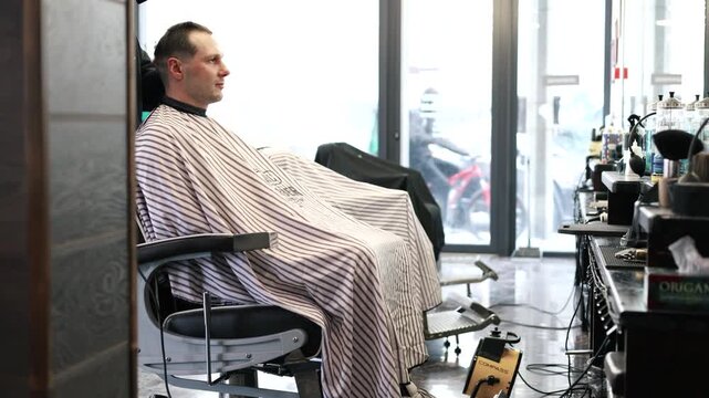 A young male Barber adjusts the hair of a male client. Professional hair care products. Cinematic close-up of a barber giving fade haircut to male client. Slow motion shot of short clipper hairstyle.