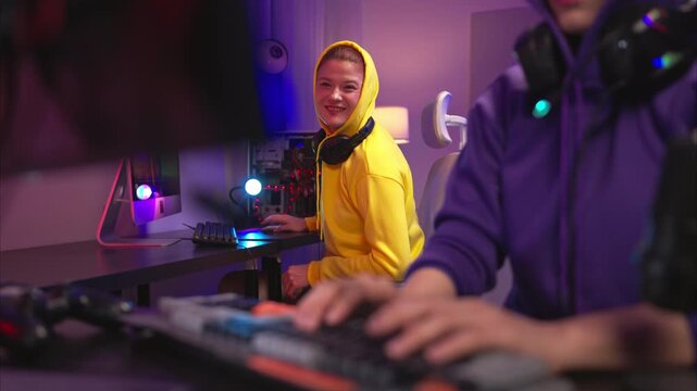 Two woman gamers wearing headsets playing a video game together in a colorful gaming room. They are holding game controllers, interacting with the screen, and enjoying an exciting multiplayer session