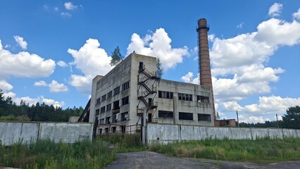 abandoned factory atmosphere, a deserted industrial building in a grassy area, with weathered features and a tall brick chimney, sits beneath a bright sky © Industrial Supplier