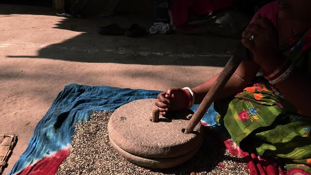 A close-up view of an Indian woman working with a stone quern to grind urad dal highlights traditional village life, sustainable living, and authentic culinary heritage.