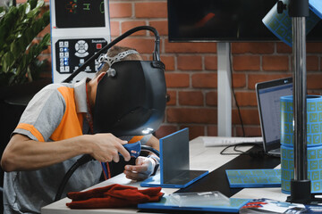 welder concentrating on forming clean weld seam at fabrication workstation. Welder in protective helmet performing manual welding process