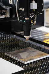 CNC fiber laser cutting head positioned above sheet metal on lamella support table with slats for precise contour cutting