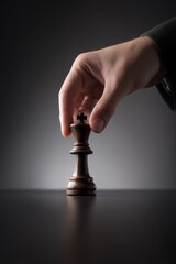 Mano colocando una figura de rey de ajedrez de madera, Imagen para campa&ntilde;a de liderazgo empresarial, Figura de ajedrez de rey sostenida con la mano sobre fondo oscuro