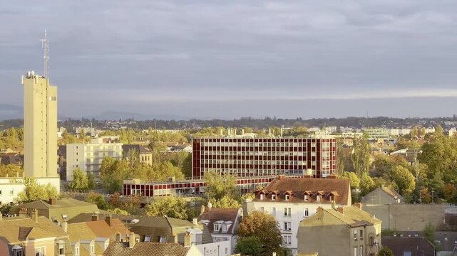 Fire station barracks with red modern facade and rooftop antennas, Alsace cityscape at golden hour, autumn trees and residential rooftops