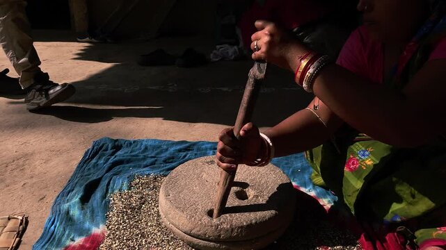 In a rural Indian household, a woman carefully grinds black gram lentils using a traditional hand-operated millstone, preserving age-old food preparation methods passed down through generations.
