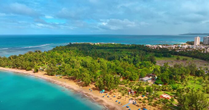 Flight over the turquoise waterscape approaching the sandy beach with lots of greenery. Vast blue seascape at backdrop. Puerto Rico.