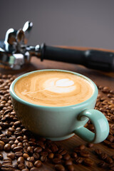 A cup of cappuccino coffee with a foam pattern, top view. Coffee beans and cinnamon sticks are scattered around it.                              