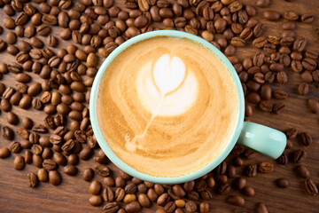 A cup of cappuccino coffee with a foam pattern, top view. Coffee beans are scattered around it.                  