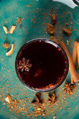 A cup of tea stands on a plate with cinnamon sticks and cloves, top view                           