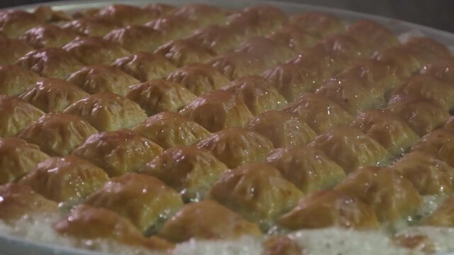 Close-up 10-bit slow motion of boiling sugar syrup poured over golden square baklava. Capturing the aromatic steam and bubbling texture of the authentic Gaziantep recipe. High-quality 4K.
