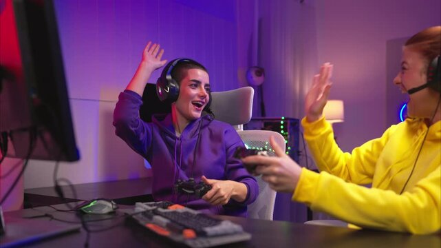 Two woman gamers wearing headsets playing a video game together in a colorful gaming room. They are holding game controllers, interacting with the screen, and enjoying an exciting multiplayer session