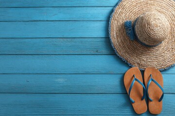 Straw hat and flip-flops on a teal wooden surface