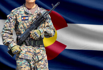 Naklejka premium Colorado US state flag with soldier in military uniform holding assault rifle in front of it