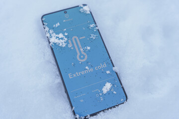 Smartphone screen showing low temperature thermometer lying in snow outdoors, extreme cold concept