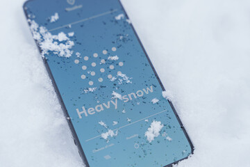 Smartphone lying in heavy snow outdoors with weather app screen showing snow forecast