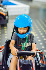 Seven-year-old Asian boy driving a go-kart at an indoor racing track in high-end hotel