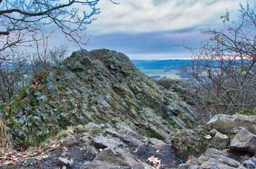 Surowe kamienne ruiny z widokiem na dolinę ze szlaku górskiego o zmierzchu, wśród nagich drzew i szerokiego nieba - późna jesień w rezerwacie przyrody „Ostrzyca Proboszczowicka”. © Pol Badger
