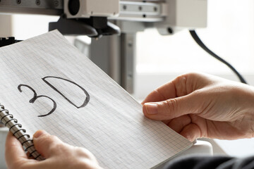 A girl holding a desktop 3D printer and a notebook with the word "3D" written on it, additive manufacturing technologies