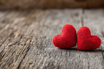 Two small red fabric hearts rest side by side on weathered wooden planks, symbolizing simple, heartfelt love in a cozy and rustic setting