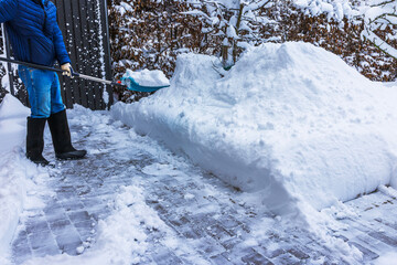 Close up view of person removing deep snow from villa driveway using shovel during cold winter day. Sweden.