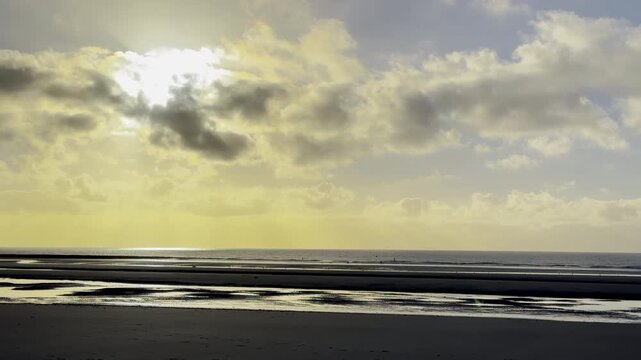 Golden sunset sky with dramatic clouds over calm sea and low tide beach, shimmering reflections on wet sand and tidal flats, peaceful coastal seascape in France