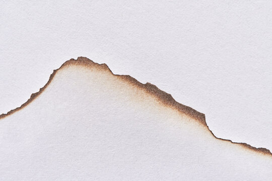 Torn paper edge with burn marks creating rugged shapes on white background.
