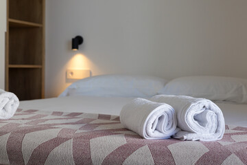 Close-up of rolled white towels on neatly made hotel bed with patterned blanket