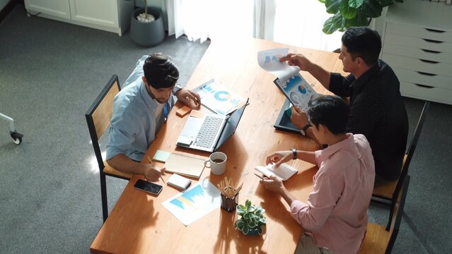 Executive manager explain financial graph to colleague at meeting room. Top aerial view of diverse marketing team sharing idea and planning strategy while sitting at table with tablet. Convocation. - Powered by Adobe