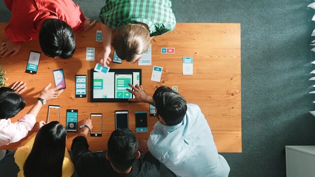 Top view of software developer team looking Ux Ui design for mobile phone interface from tablet while comparing and planning wireframe prototype designing together at creative workplace. Convocation. - Powered by Adobe