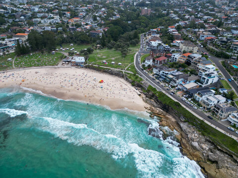 Aerial view of Bronte Beach in Sydney, Australia, with people enjoying the coastline, ocean pools and sandy shore, showcasing coastal lifestyle and summer atmosphere captured by drone