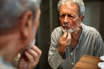Senior man inspecting beard with concerned expression in bathroom