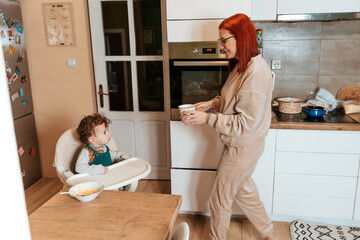 Mother Bringing a Glass of Water to Her Toddler in the Kitchen
