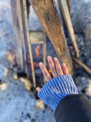 Kartepe, Turkey &ndash; January 3, 2026: Hand warming near a small campfire among wooden logs on snowy ground during cold winter weather.