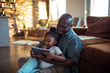 Senior grandfather and child granddaughter laughing using tablet in living room