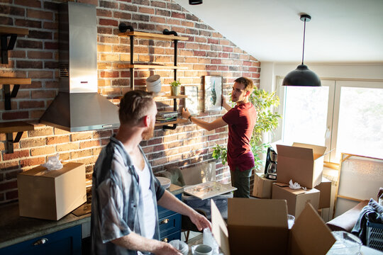 Young adult gay couple unpacking and decorating in modern kitchen, focused