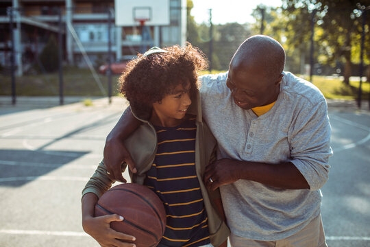 Adult father and young son smiling on outdoor basketball court