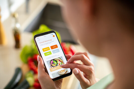 Young adult woman focused on using meal planning app in home kitchen