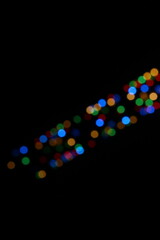 A bokeh effect photograph of multicolour circle fairy lights against a black background.