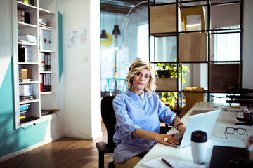 Adult woman with calm expression working on laptop in modern office