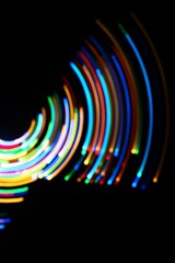 A long exposure photograph. Light painting photography; vibrant multicolour fairy lights in a circle swirl pattern against a black background