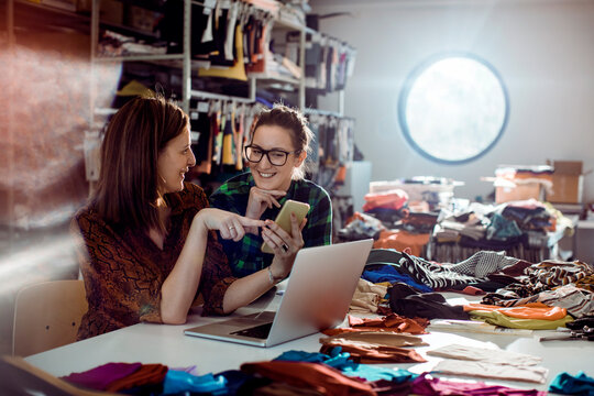 Adult women smiling and collaborating on phone in fashion studio