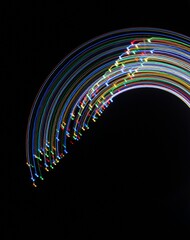A long exposure photograph. Light painting photography; vibrant multicolour fairy lights in a circle swirl pattern against a black background