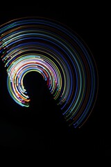 A long exposure photograph. Light painting photography; vibrant multicolour fairy lights in a circle swirl pattern against a black background