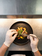 Chef Plating Gourmet Dish with Tweezers on Stainless Steel Counter