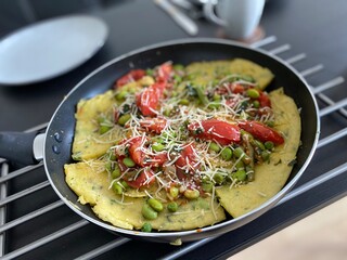 Vegetable omelette with tomatoes, green beans and cheese in frying pan; homemade vegetable omelette cooked in a frying pan, topped with cherry tomatoes, green beans, peas and grated cheese