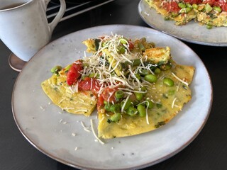 Vegetable omelette slice with tomatoes, peas and cheese on plate; a homemade vegetable omelette served on a ceramic plate, topped with tomatoes, green peas and grated cheese